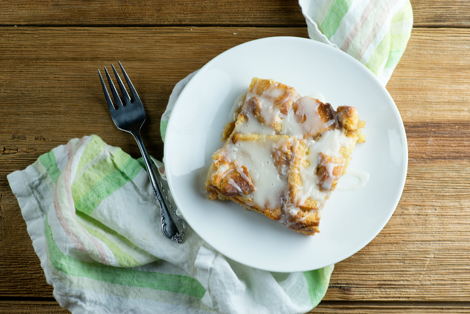 Cinnamon roll bread pudding on a plate with a fork on the side.