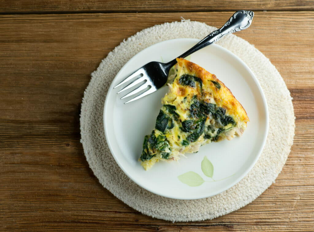 Slice of chicken spinach frittata on a plate with a fork.
