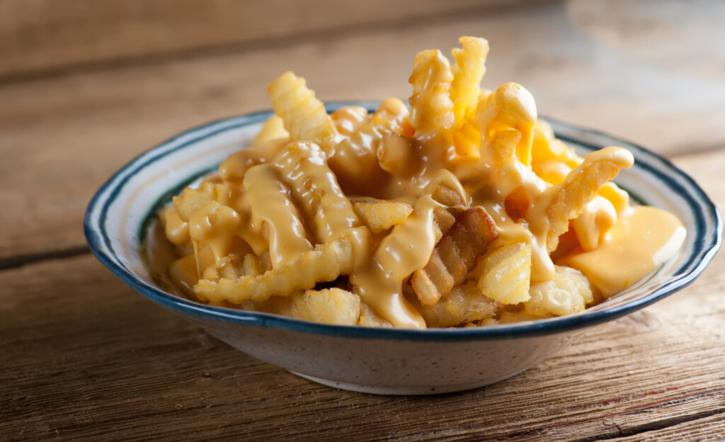 Cheese fries in a bowl on a wodden counter.