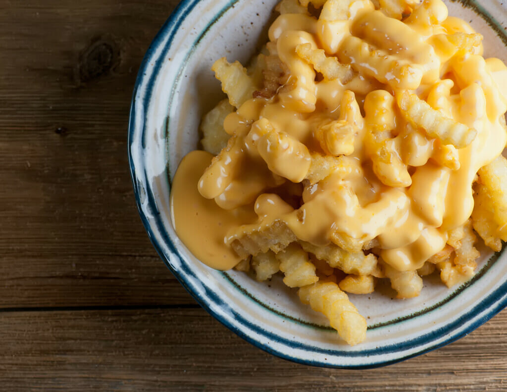 Cheese Fries in a bowl on a wooden counter.