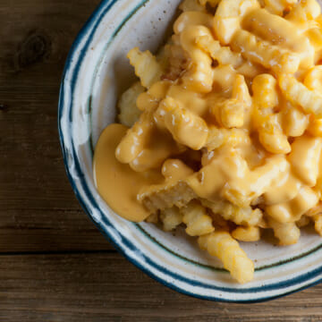 Cheese Fries in a bowl on a wooden counter.