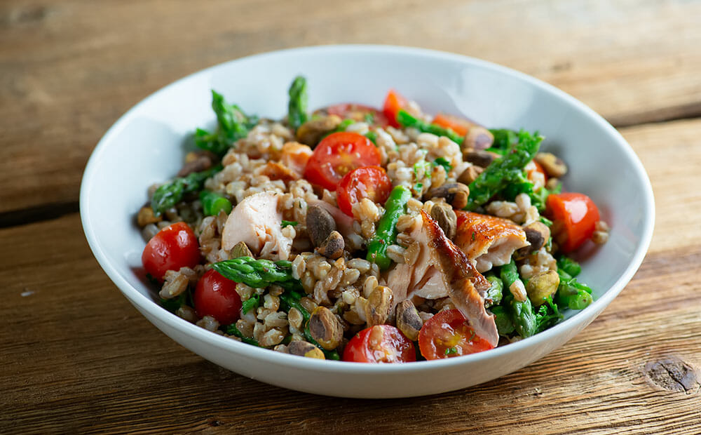 Finished roasted salmon grain bowl with salmon, farro, tomatoes, asparagus nuts and dressing.