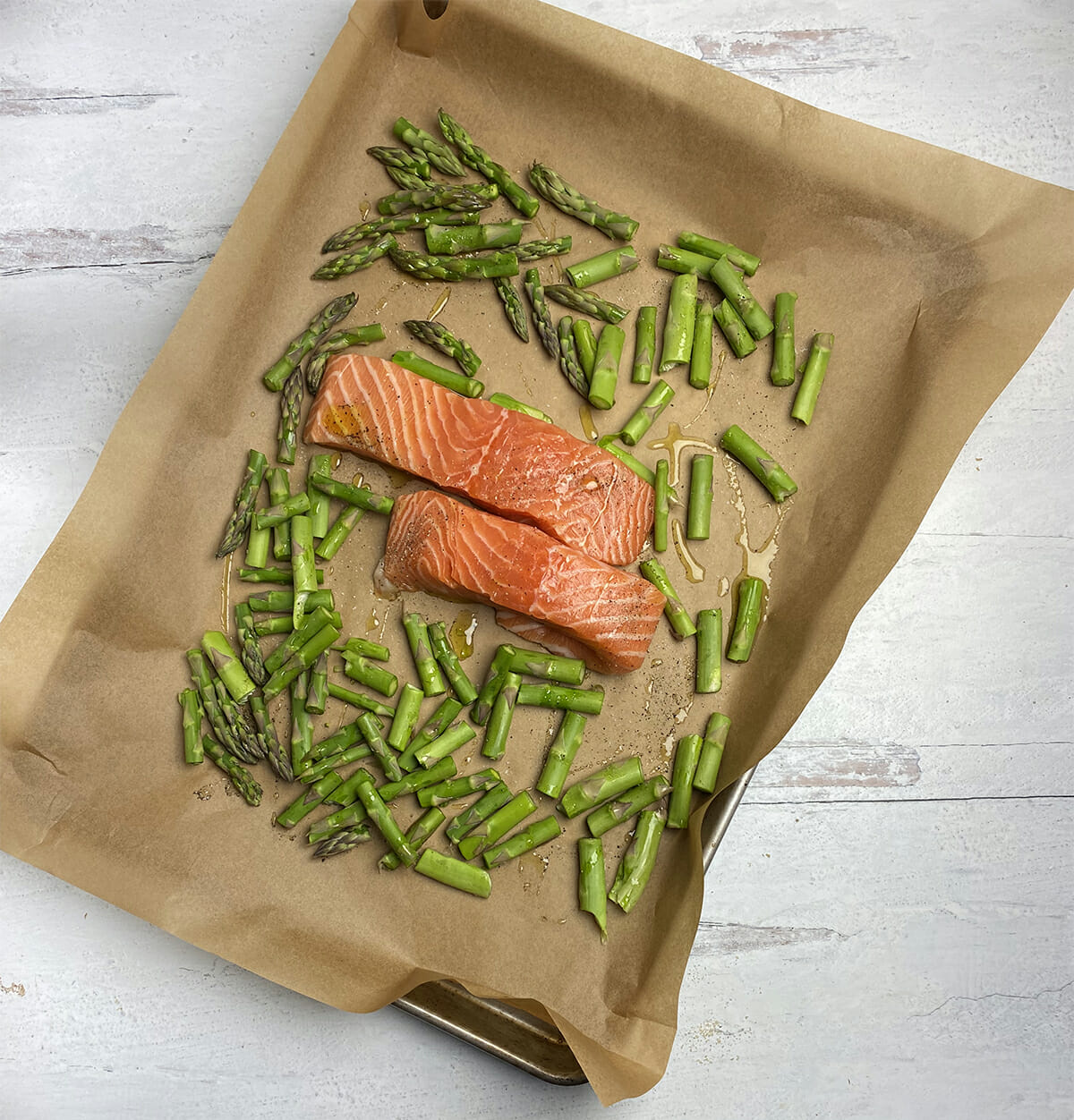 Salmon filets and cut up asparagus on a baking sheet covered with parchment paper, ready for the oven.