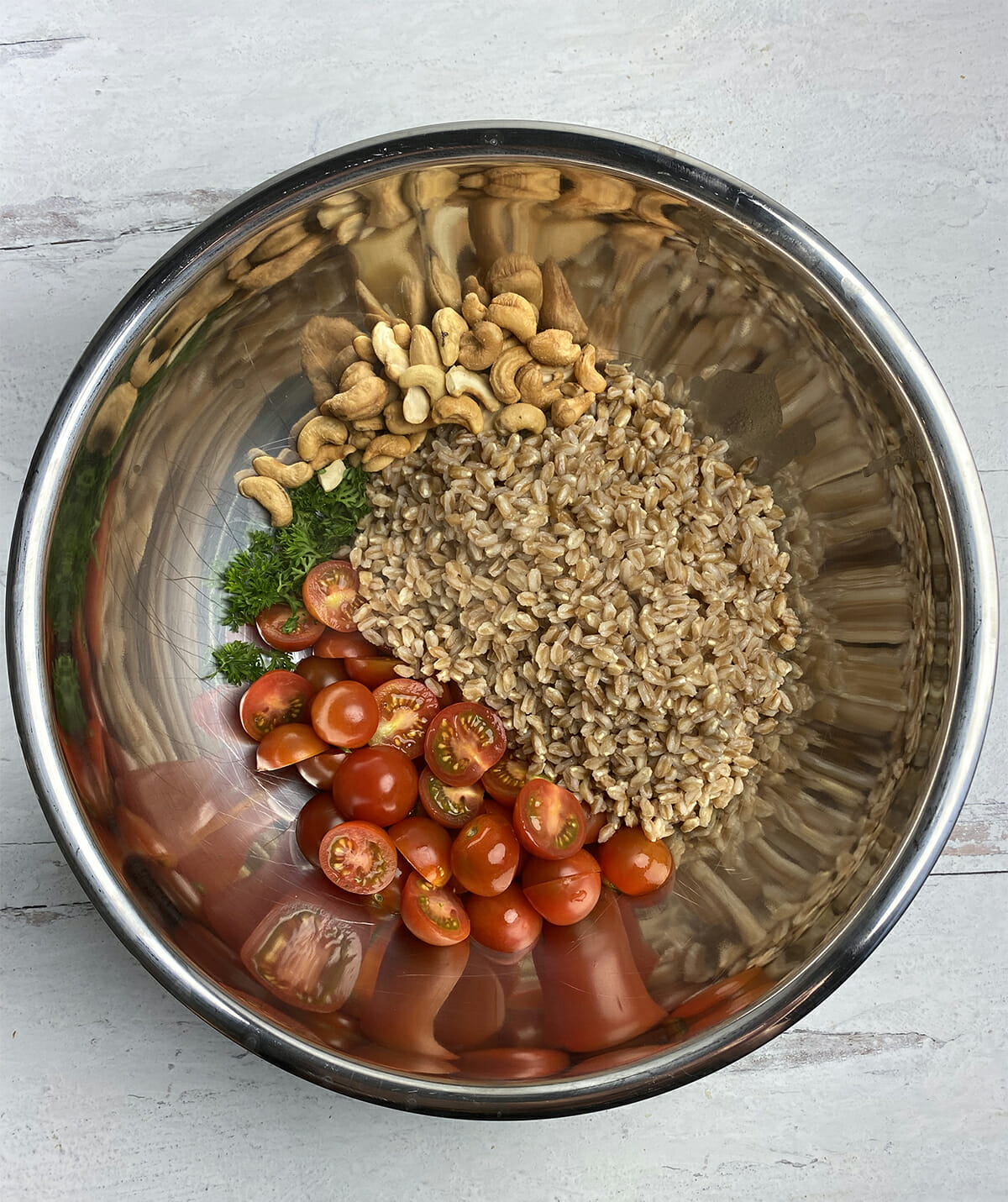 Mixing bowl with cooked farro, cherry tomatoes, parsley and nuts.