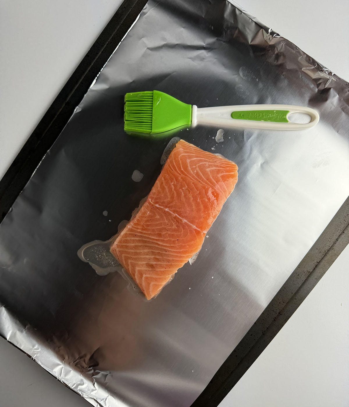 Salmon filet on a baking sheet with a pastry brush.