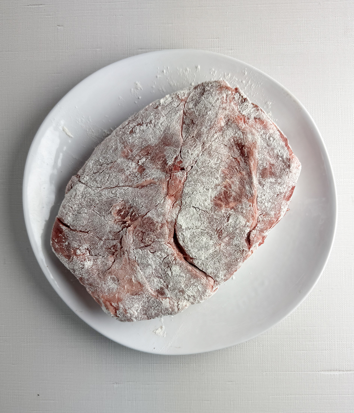 Chuck roast coated with flour on a plate.