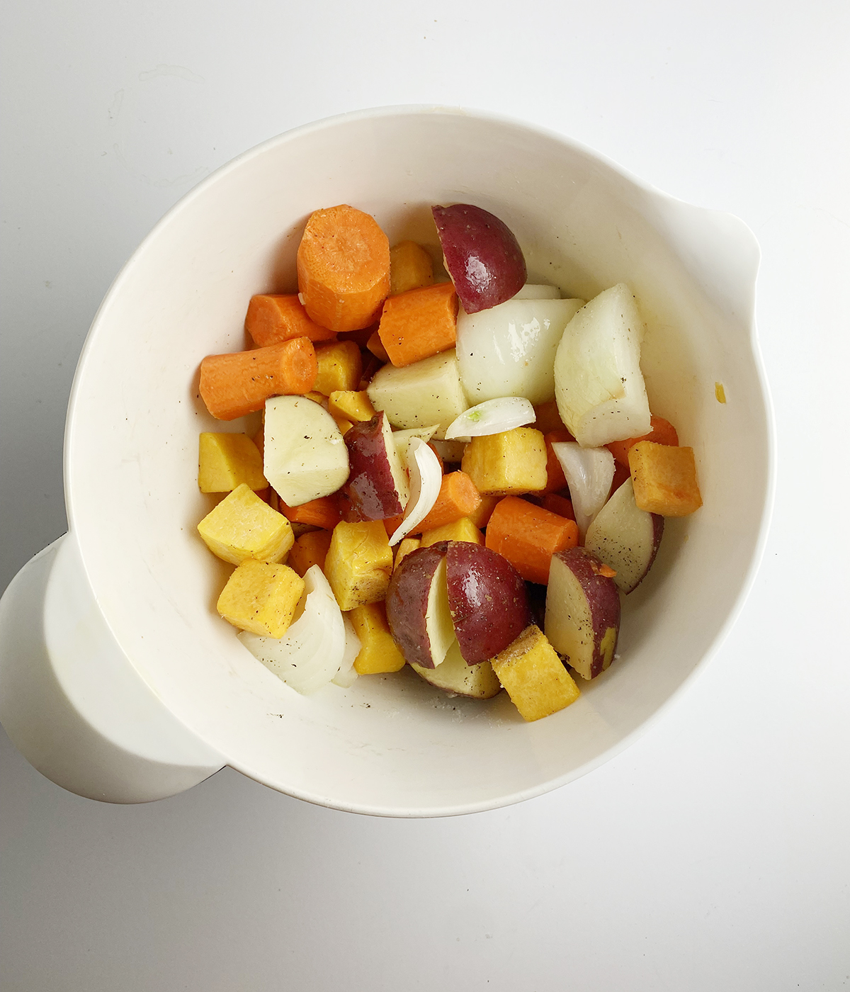 Fall vegetables tossed with olive oil in a mixing bowl.