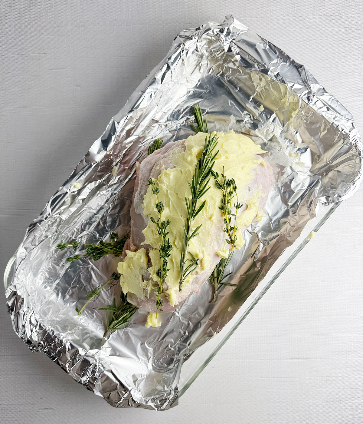 Turkey breast coated with butter and herbs in a roasting pan.