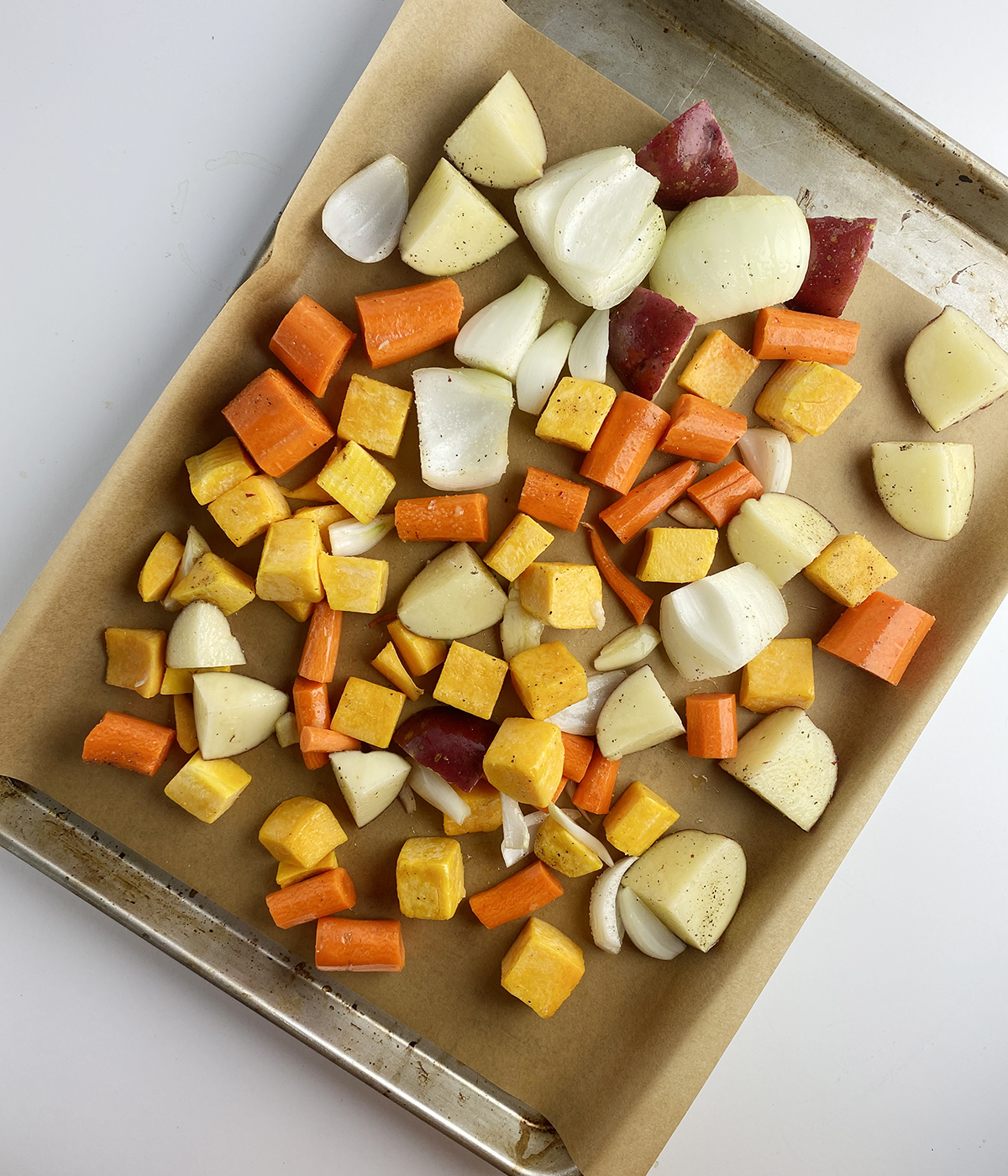 Uncooked fall vegetables on a baking pan lined with parchment.