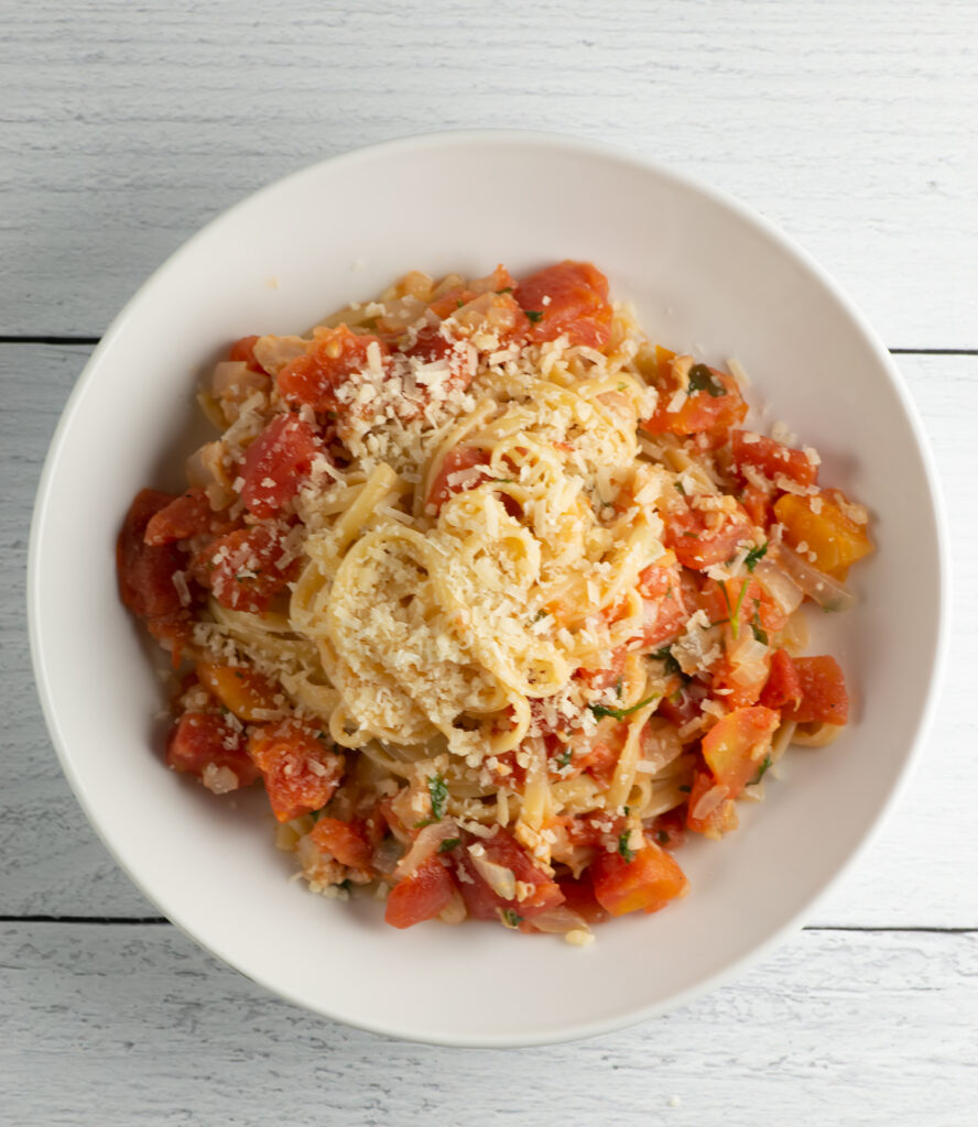 A bowl of pasta with Clam Marinara Sauce on a wooden counter.