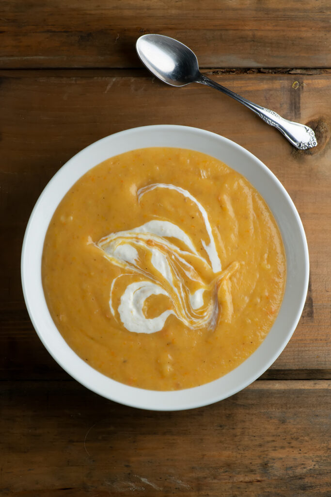 Winter vegetable soup with a sour cream horseradish drizzle in a bowl on a wooden coounter.