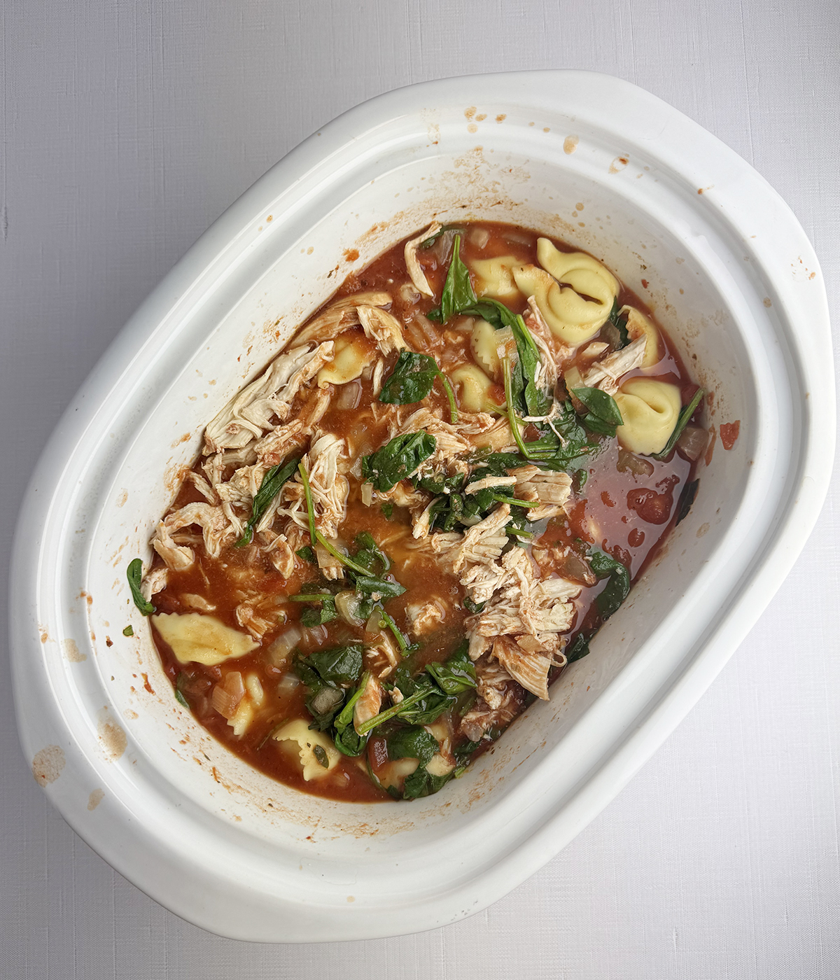 Cooked chicken tortellini soup in a slow cooker.