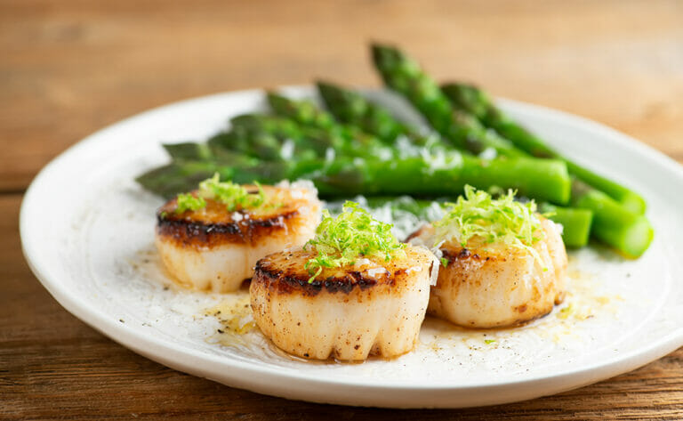 Lime parmesan scallops on a plate with asparagus.