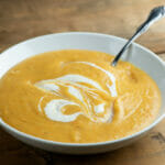 Winter vegetable soup in a bowl with a spoon on a wooden counter.