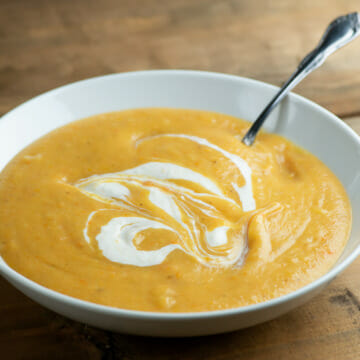 Winter vegetable soup in a bowl with a spoon on a wooden counter.