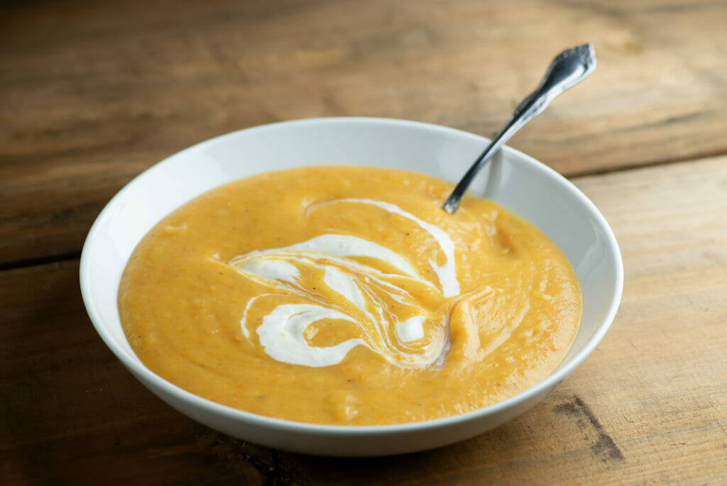 Bowl of winter vegetable soup with a spoon sitting on a wooden counter.