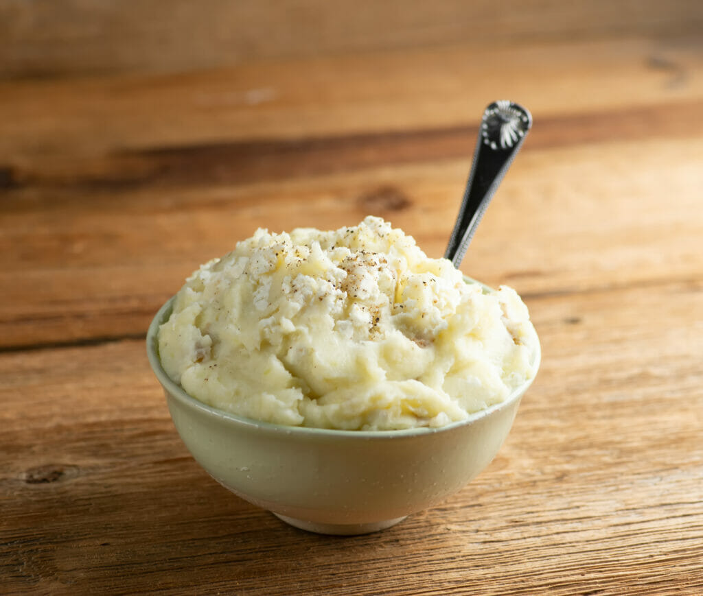 A bowl of creamy feta mashed potatoes with a spoon.