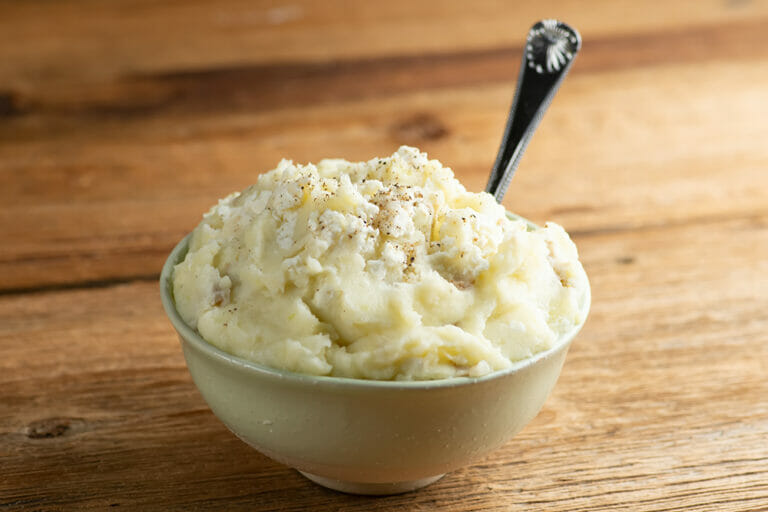 A bowl of creamy feta mashed potatoes with a spoon.