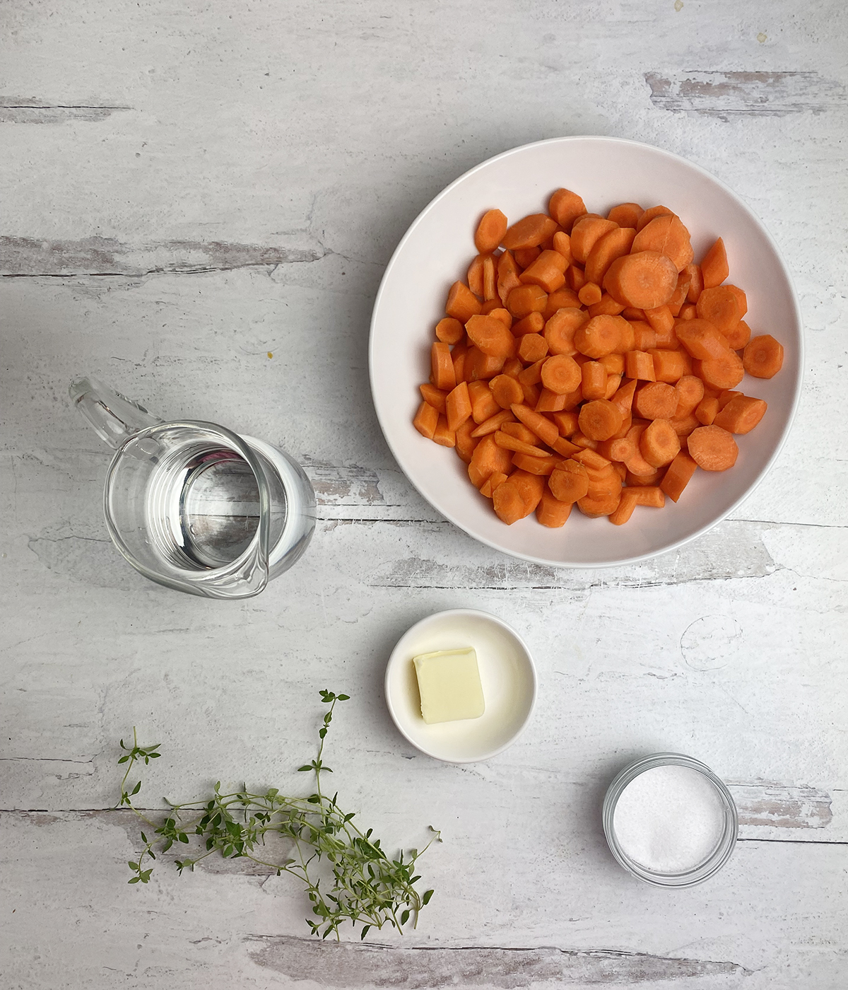 Ingredients for carrots with thyme on a wooden board.