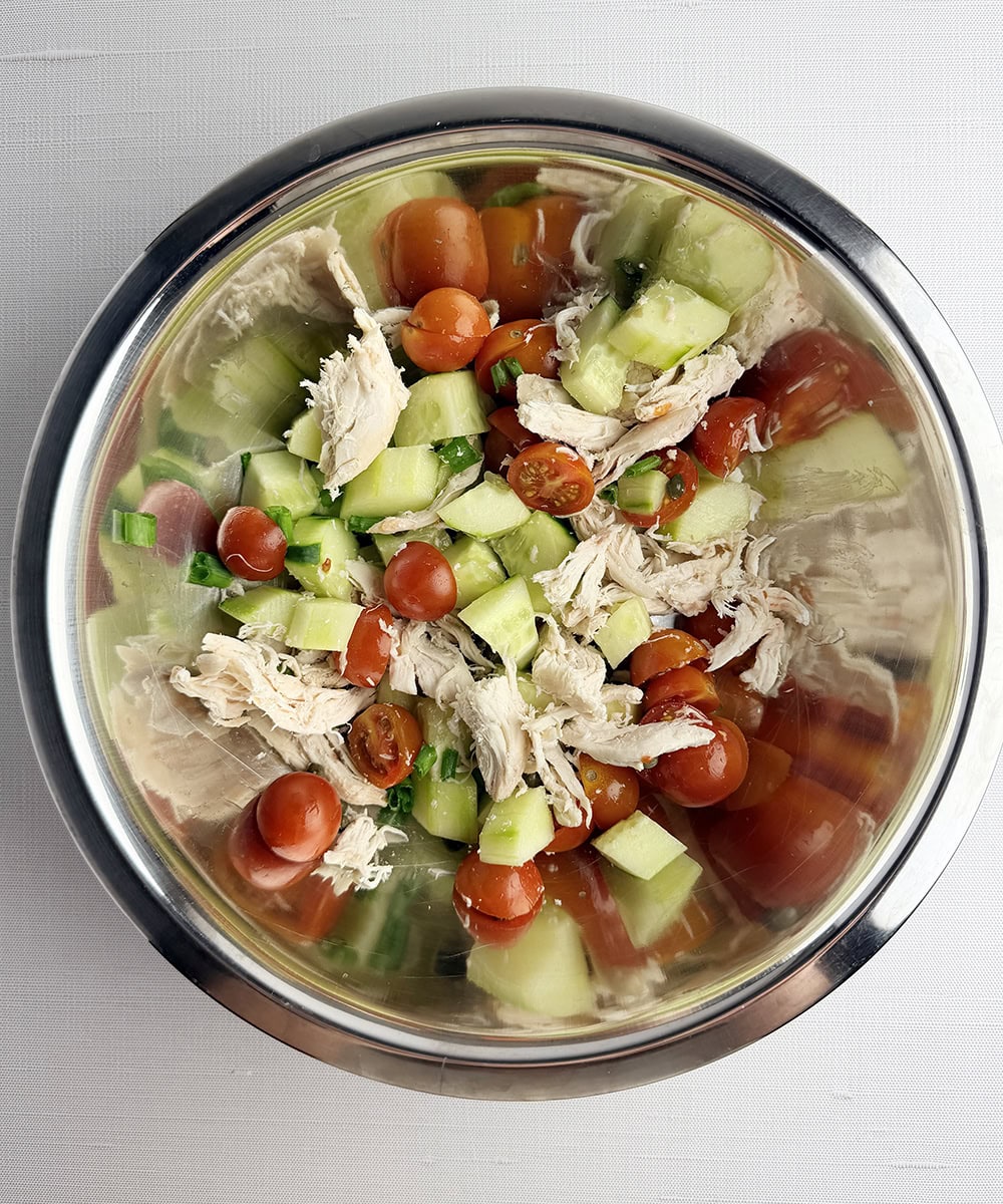 Chicken tomato and cucumber mixture in a mixing bowl.