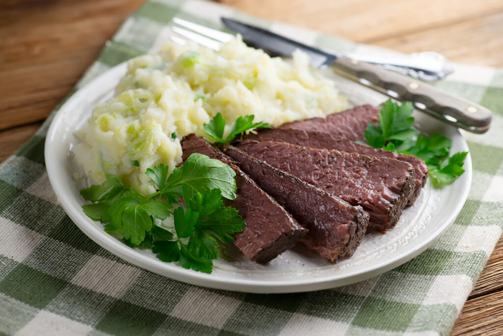 Sliced corned beef on a plate with colcannon potatoes.