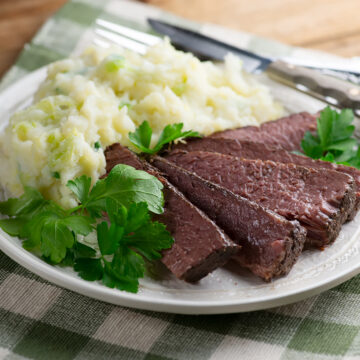 Sliced corned beef on a plate with colcannon potatoes.