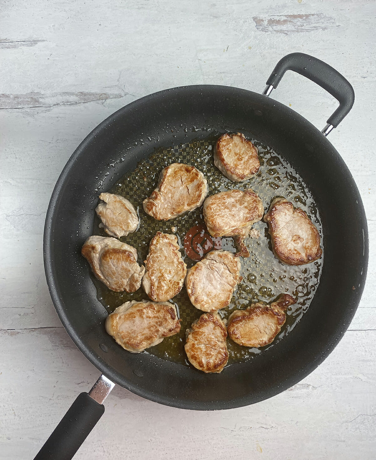 Pork medallions cooking in a skillet.