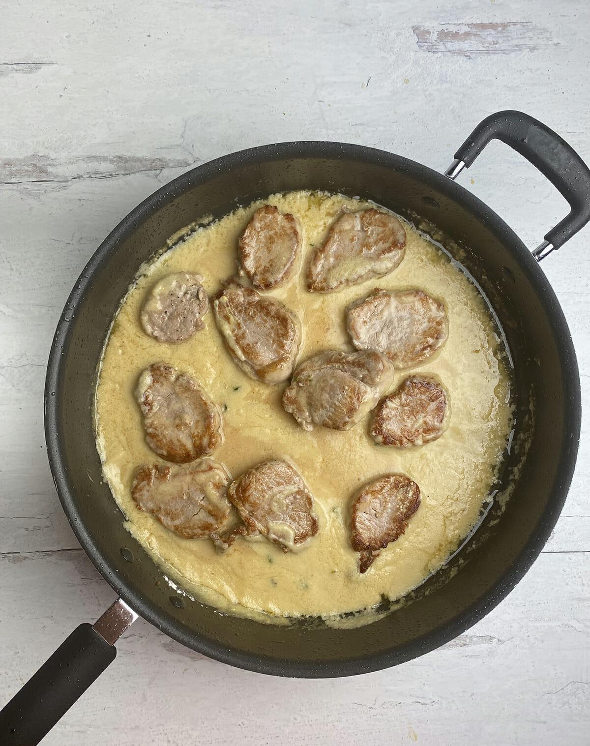 Pork medallions in sauce in a skillet.