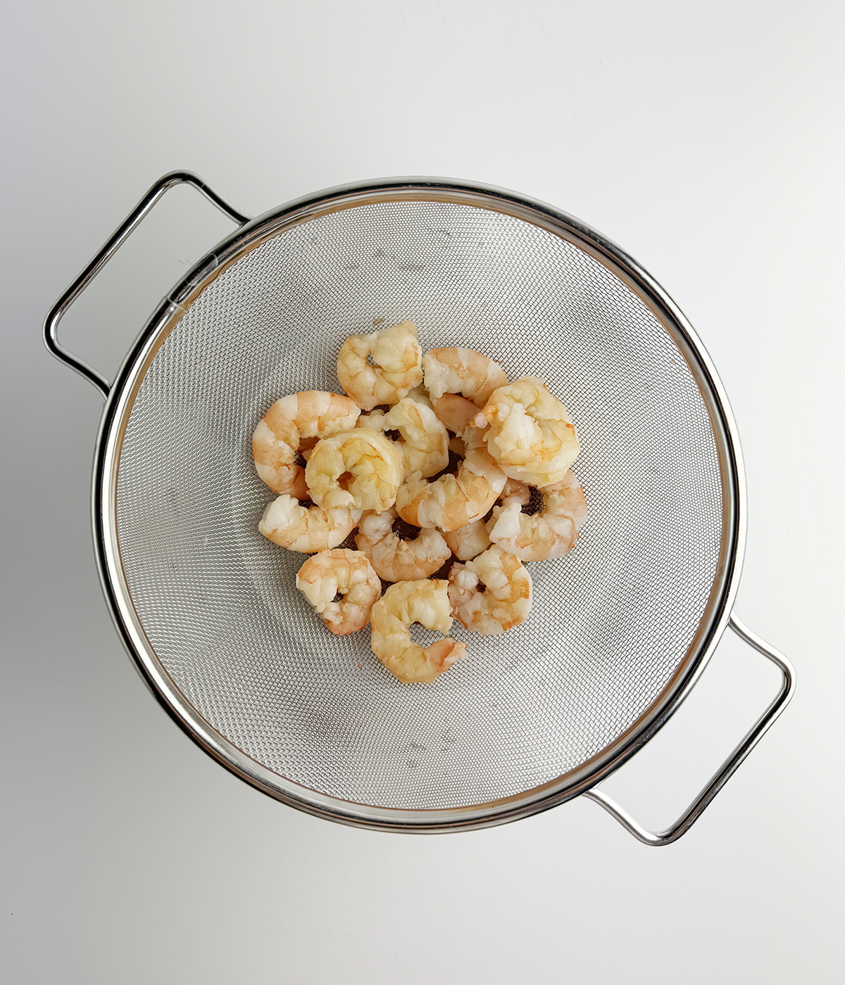Cooked shrimp draining in a strainer.