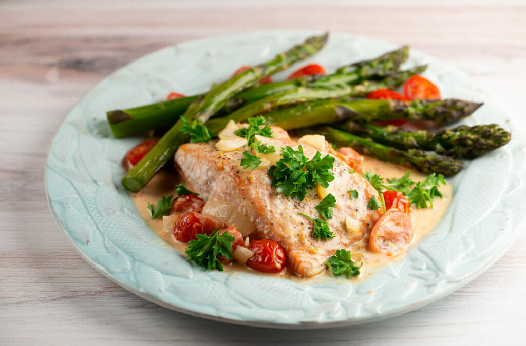 Roasted salmon with creamy tomato sauce on a plate.