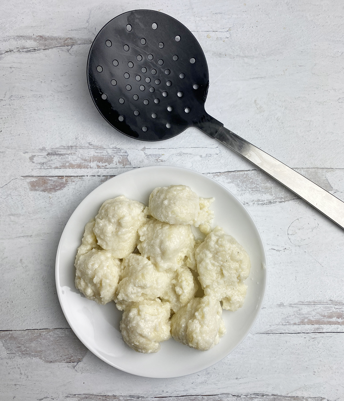 Cooked ricotta dumplings on a plate with a slotted spoon nearby.