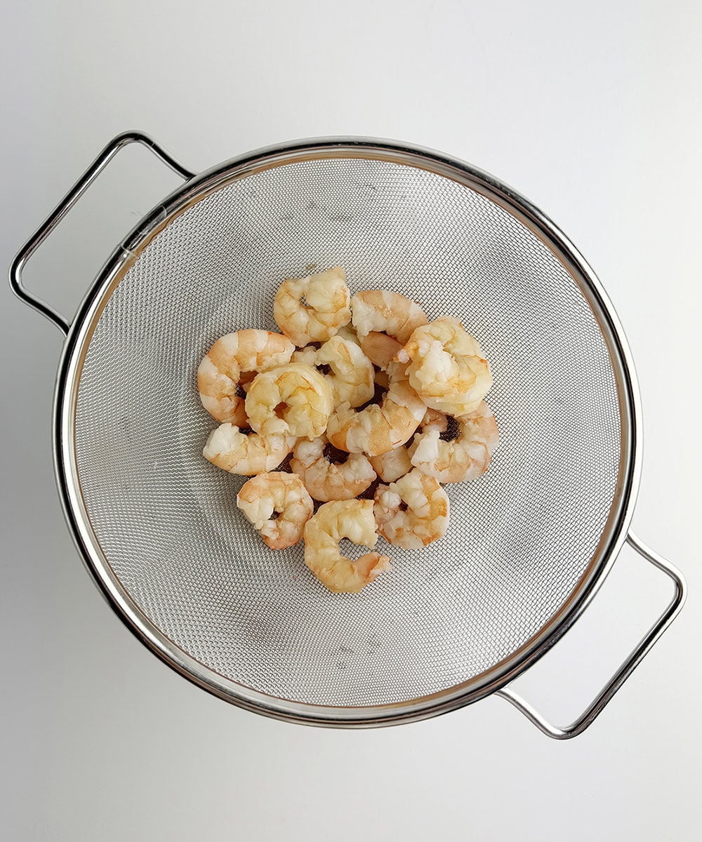 Cooked shrimp draining in a strainer.