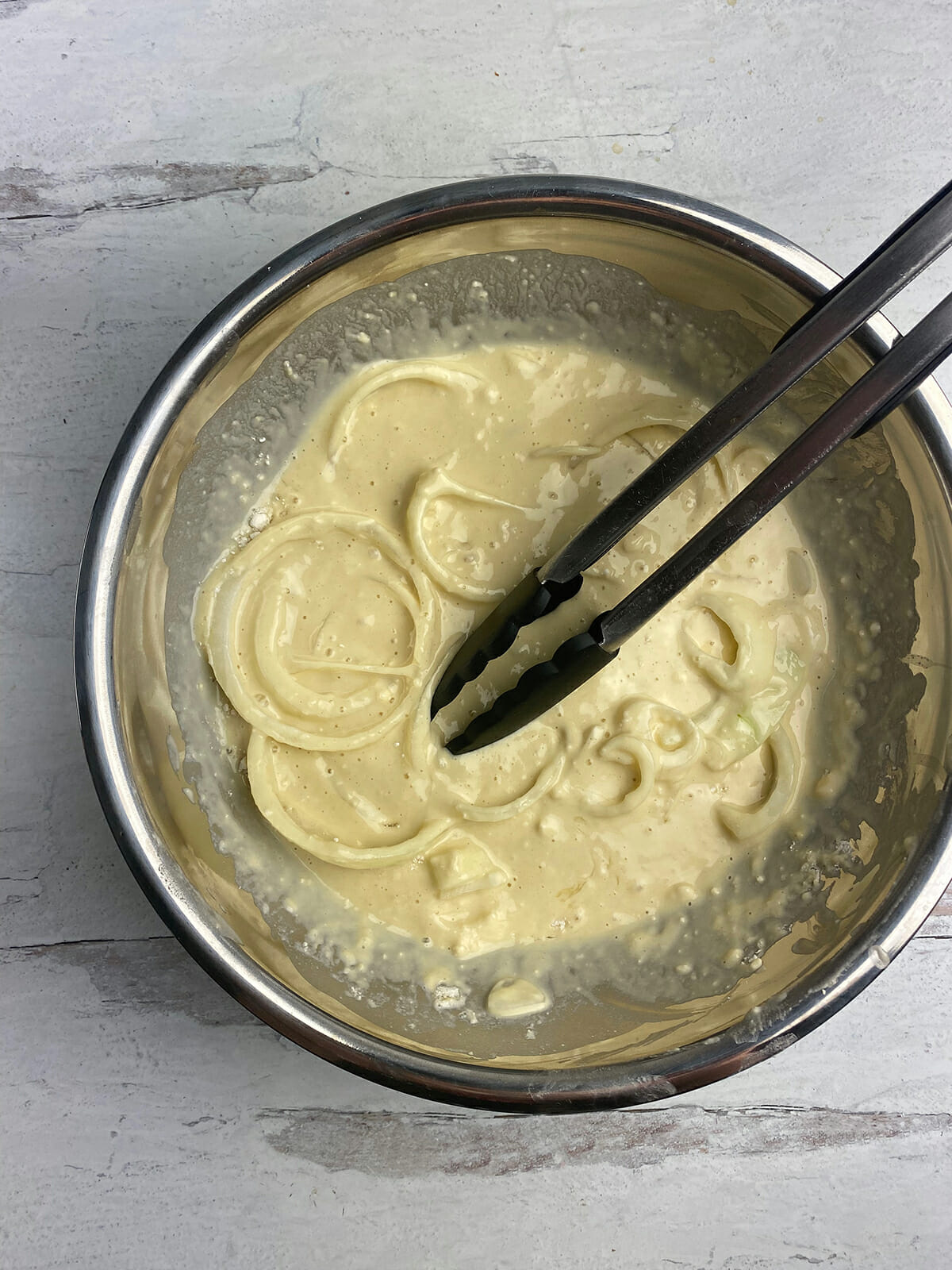 Onion slices in pancake batter in a mixing bowl.