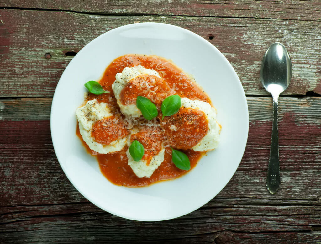 A plate of ricotta dumplings with tomato sauce and basil.