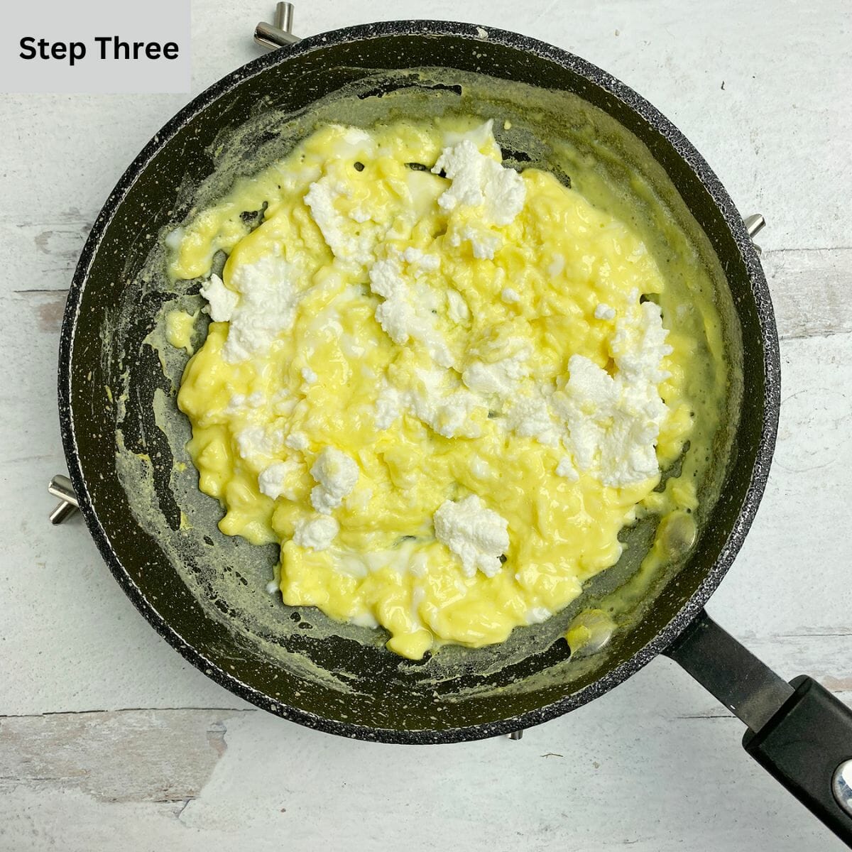 Scrambled eggs in a skillet with dollops of ricotta cheese.