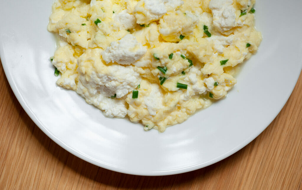 Soft scrambled eggs with ricotta cheese on a white plate.