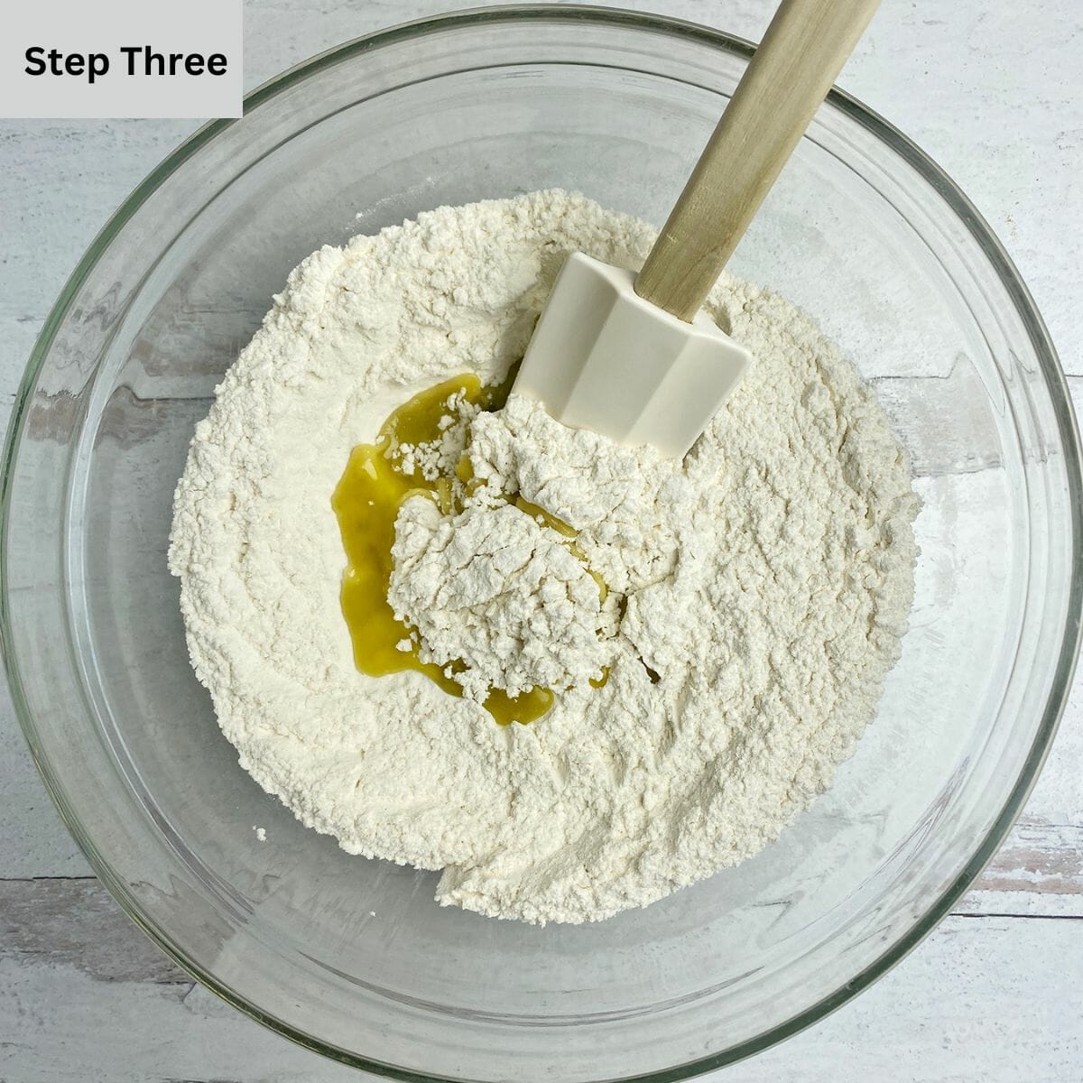 Flour and salt being mixed with olive oil in a mixing bowl.