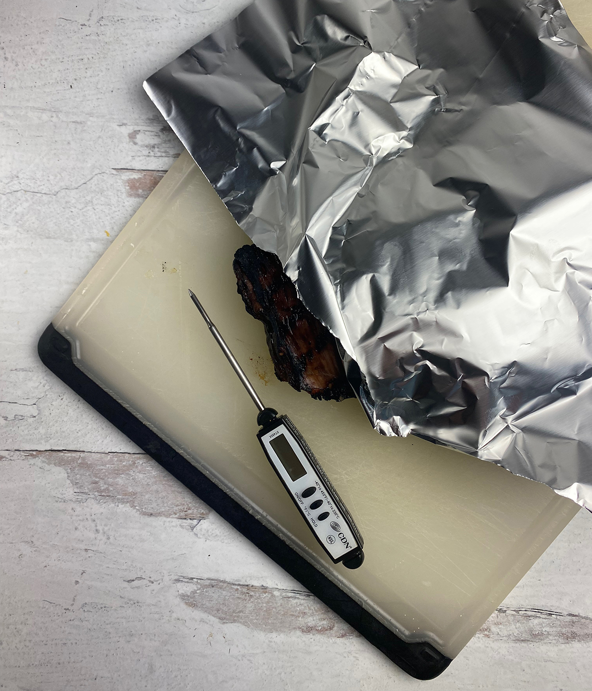 Rum steak resting under foil with a meat thermometer next to it.