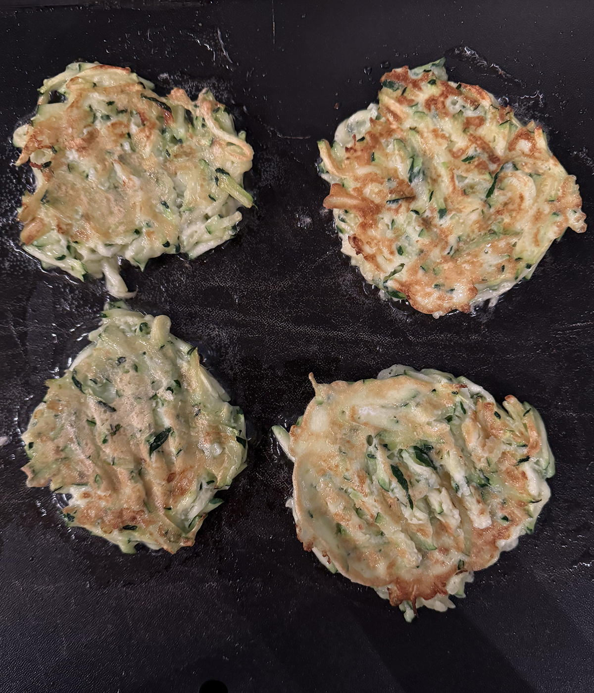 Zucchini fritters browning on the grill.