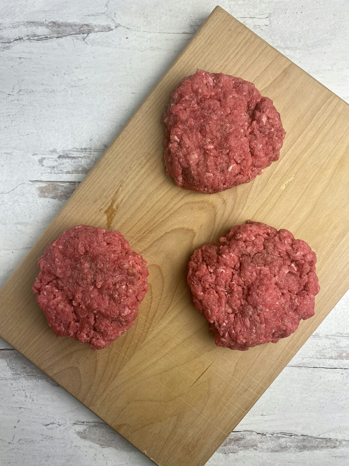 Steamed cheeseburger patties ona wooden board.