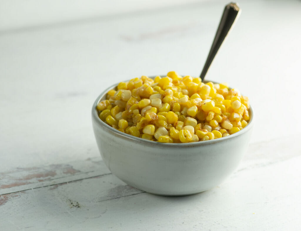 Skillet corn in a bowl with a spoon.