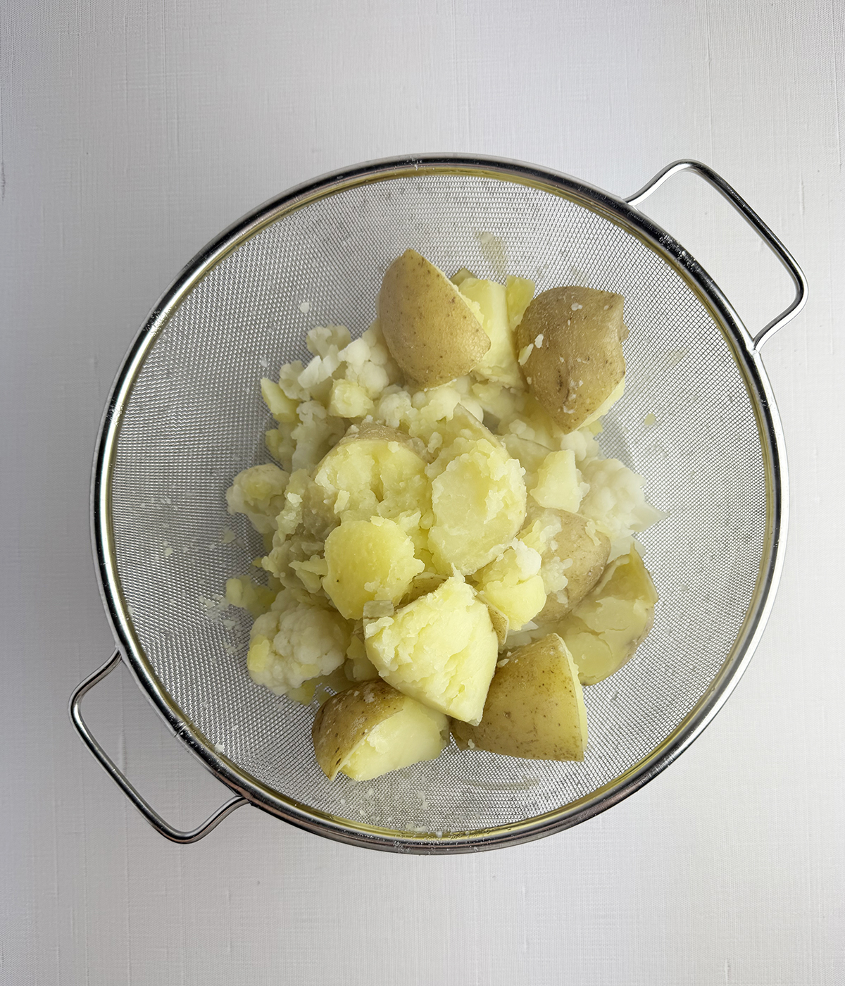 Cooked potatoes and cauliflower in a strainer.