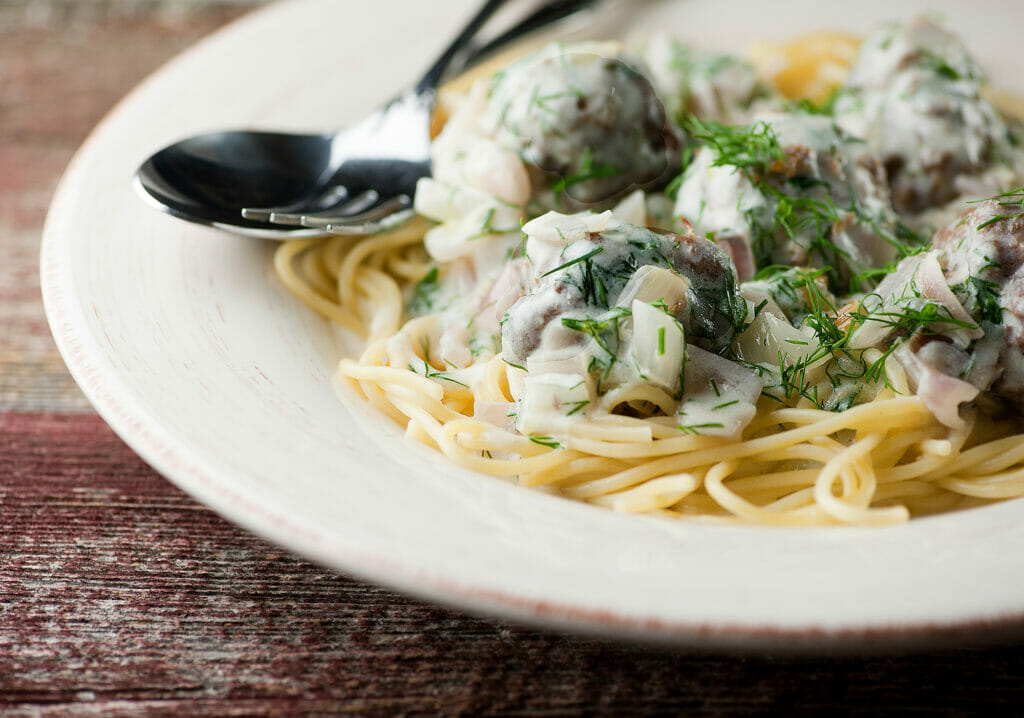 Beef Stroganoff Spaghetti and Meatballs on an plate with a fork and spoon.