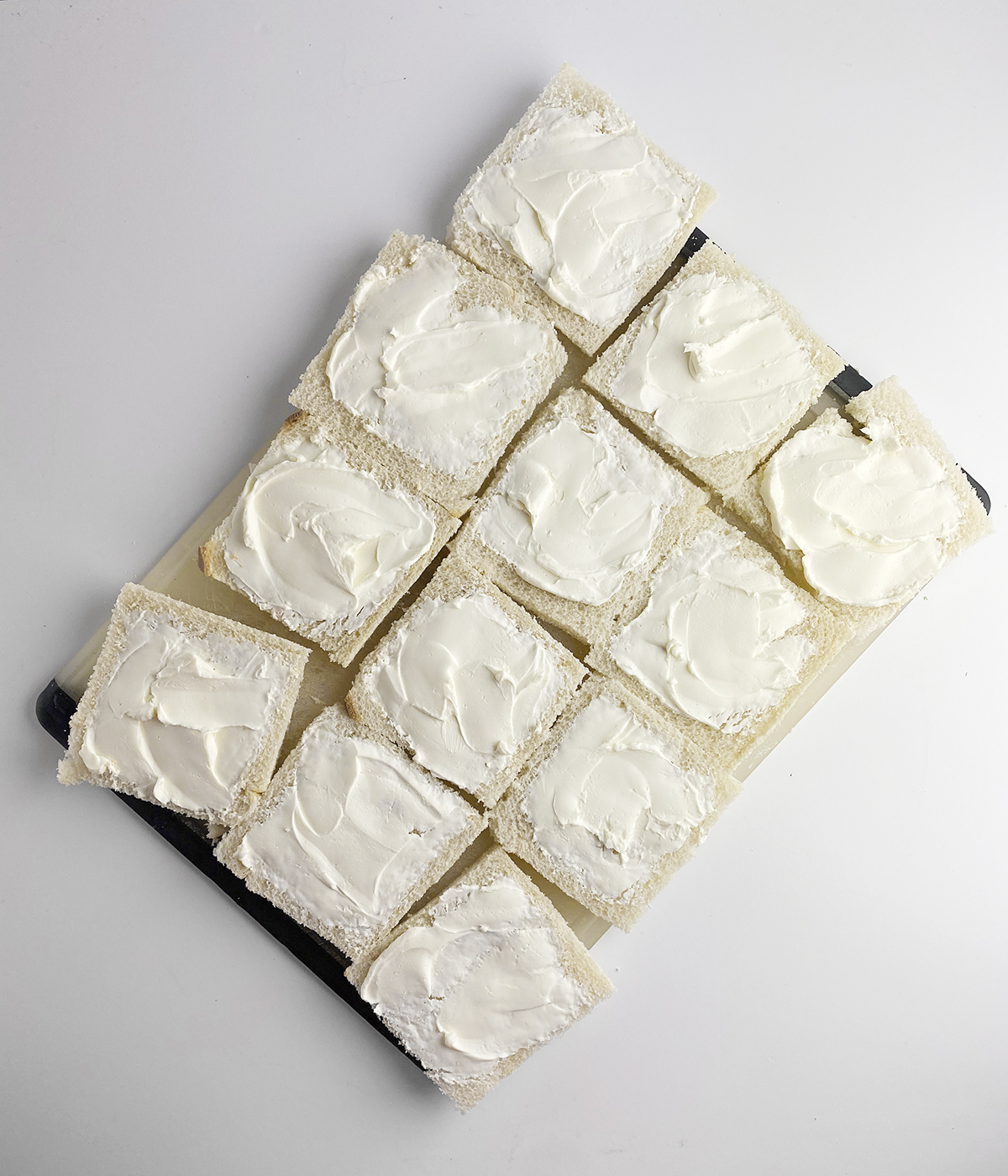 Bread slices spread with cream cheese on a cutting board.