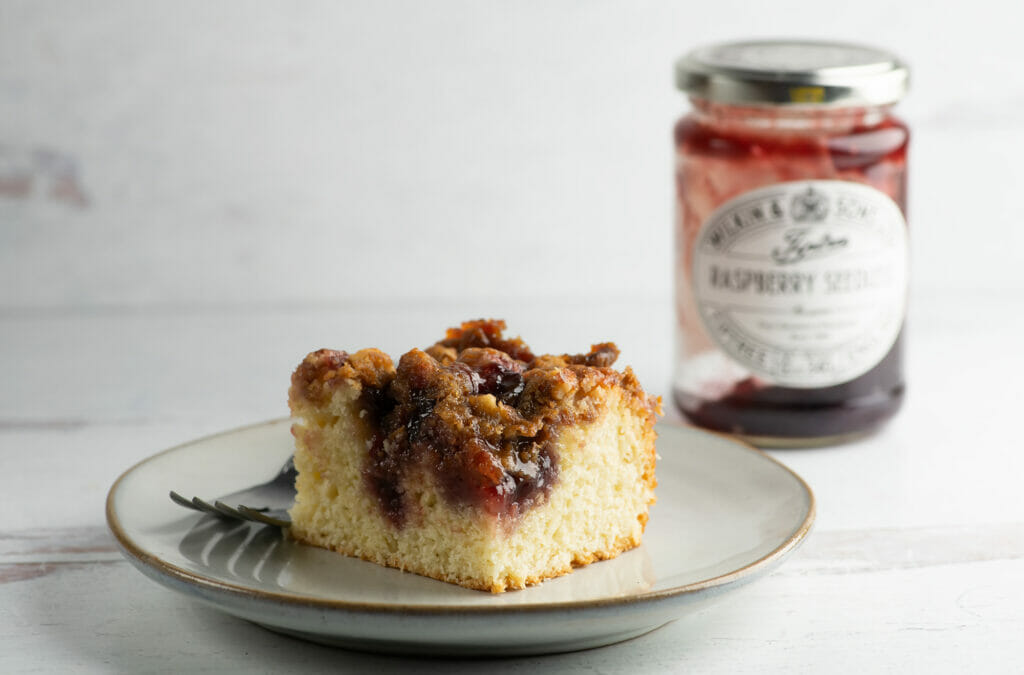 Jam cake on a plate with a fork and a jar of jam in the background.