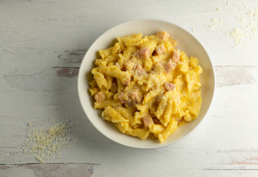 Creamy Ham Macaroni and Cheese in a bowl on a wooden counter.