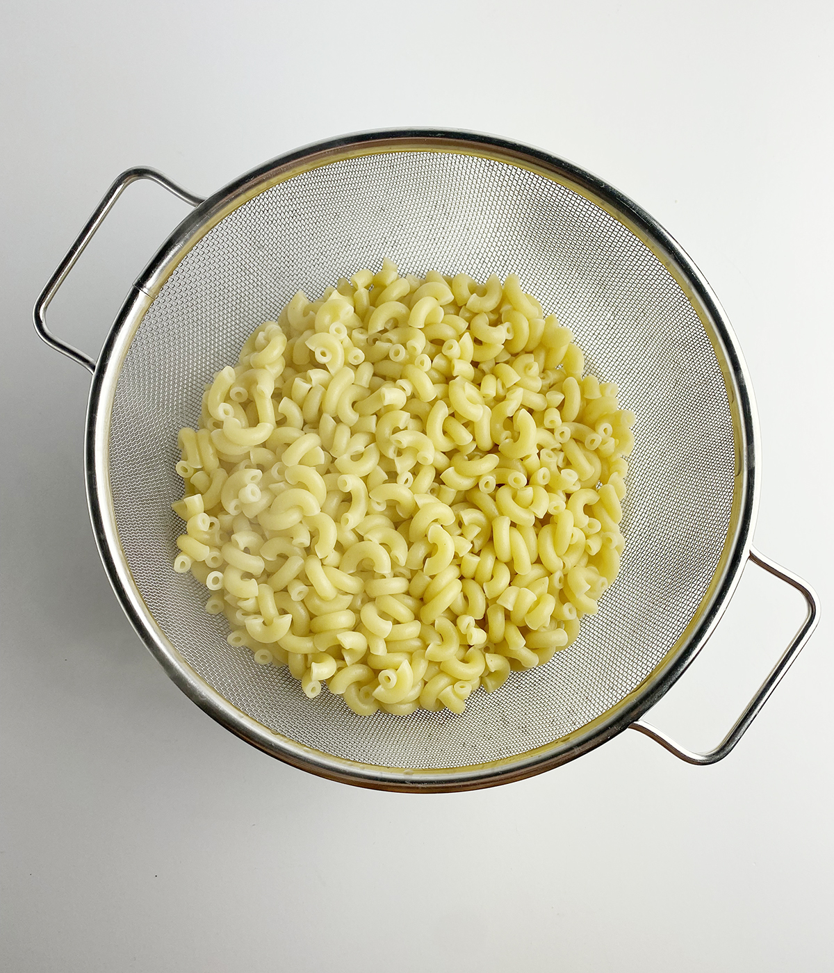 Drained elbow macaroni in a strainer.
