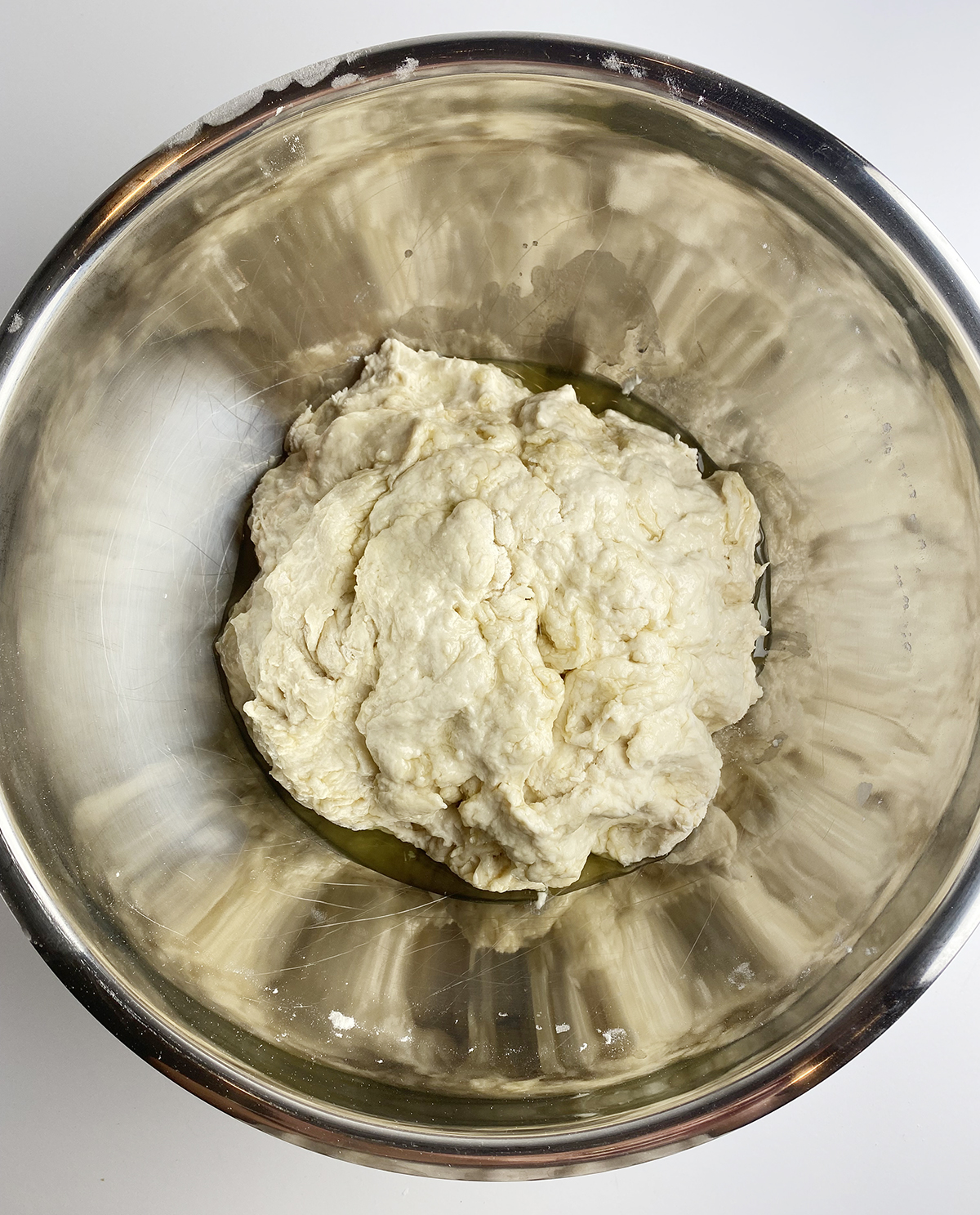 Focaccia dough with olive oil in a metal bowl.