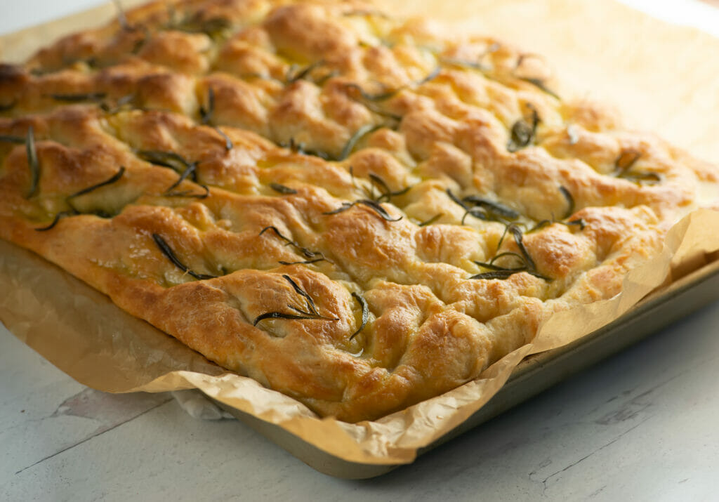 Baked focaccia in sheet pan with parchment.