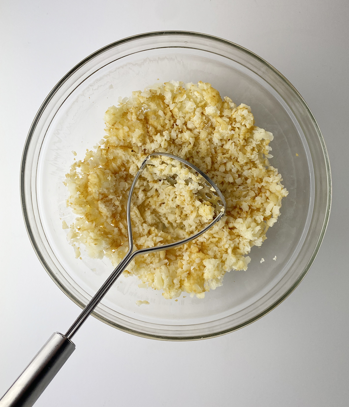 Mashing thawed Tater Tots with a potato masher.